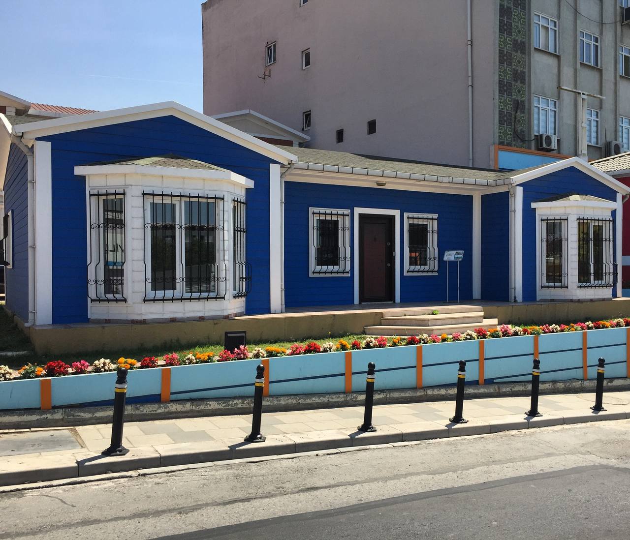 apartman yanında bulunan ve dış cephesi lacivert olan tek katlı prefabrik ev
